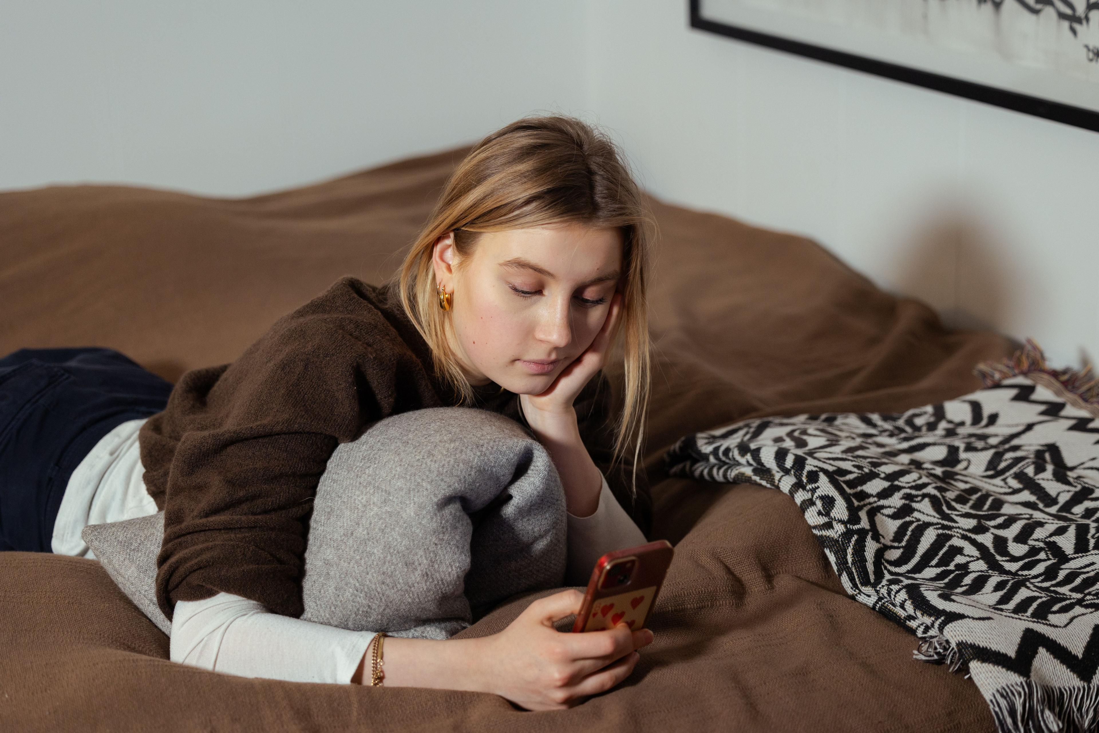 Teenager ligger i seng med smartphone